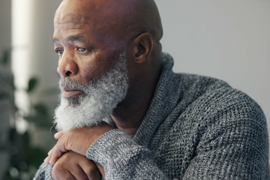 A thoughtful older man with a beard wearing a cozy gray sweater, gazing out thoughtfully.