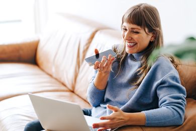 Woman smiling while on a phone call and using a laptop, sitting comfortably on a couch.